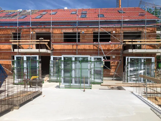 Unverputzte Fassade in Bad Füssing mit Gerüst und großen dunklen Glaselementen