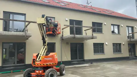 Verputzte Fassade in Bad Füssing mit Glasbalkonen und Hubarbeitsbühne